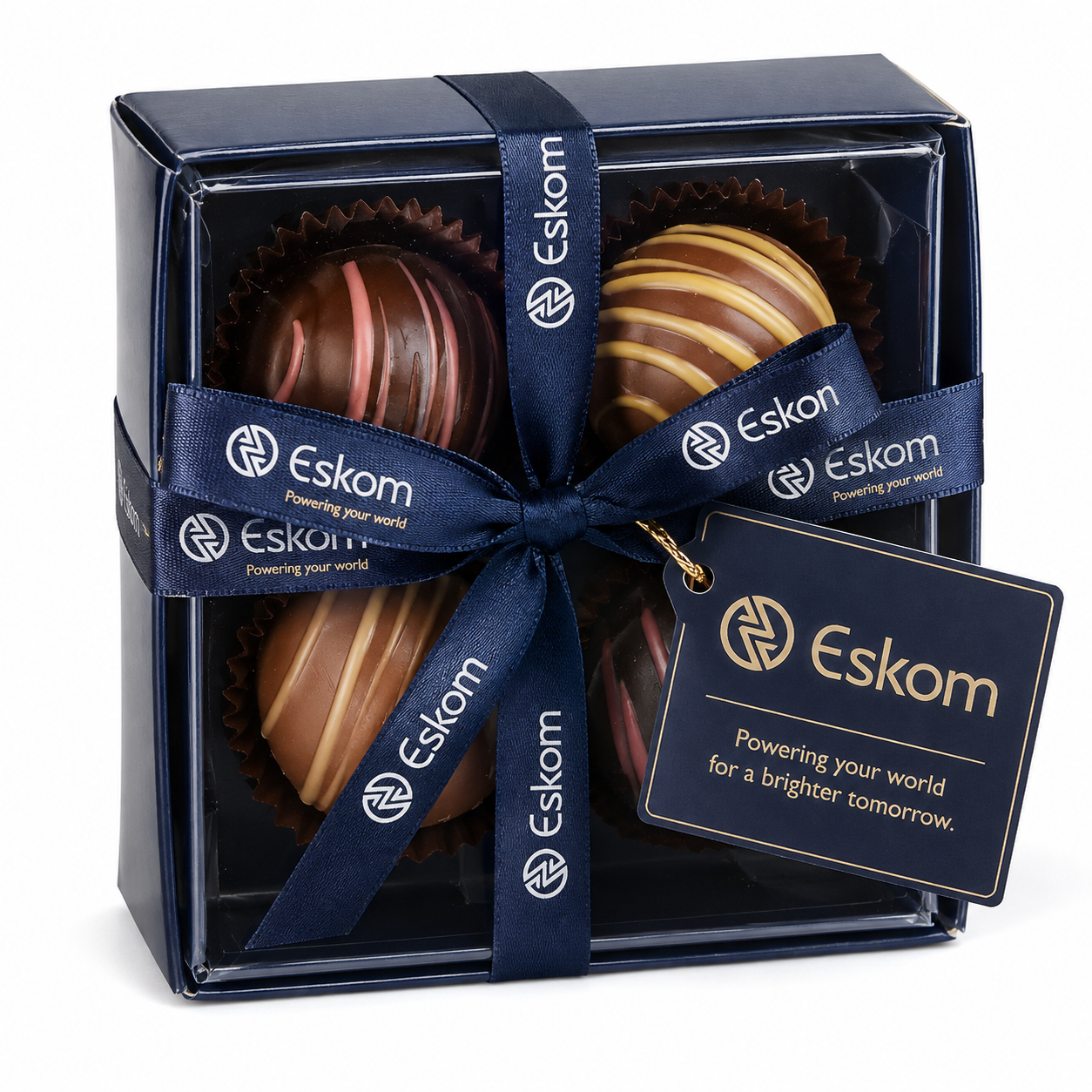 A navy gift box of four chocolate truffles tied with a wide branded satin ribbon and a matching branded gift tag, shown for Eskom