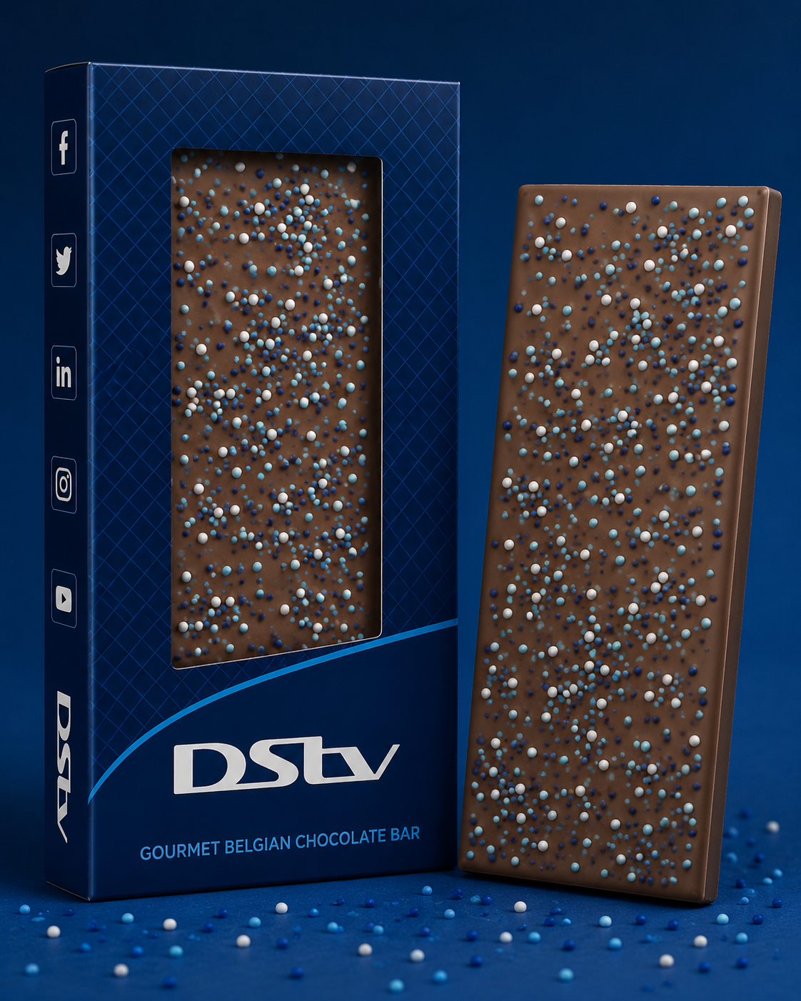 A gourmet Belgian chocolate bar topped with blue and white nonpareils, in a branded window box for DStv